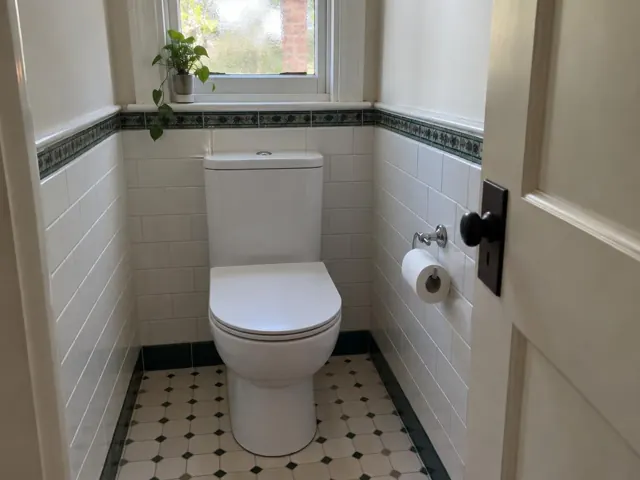 Small tiled bathroom with a white toilet, patterned floor, and open door in North Sydney